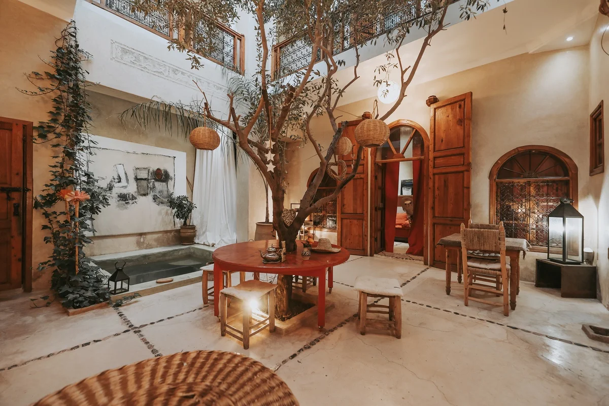 The patio of Dar Nour el Houda in the evening &mdash; one of the painter's canvases above the pool, lanterns lit beneath the olive tree