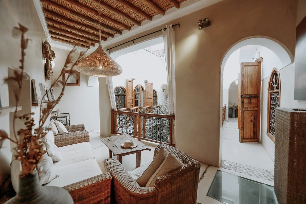 The gallery salon open to the patio — rattan sofas and white cushions beneath the beams