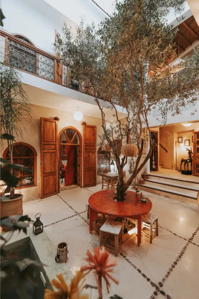 The riad's patio at nightfall — the round table beneath the olive tree, lanterns lit, warm light